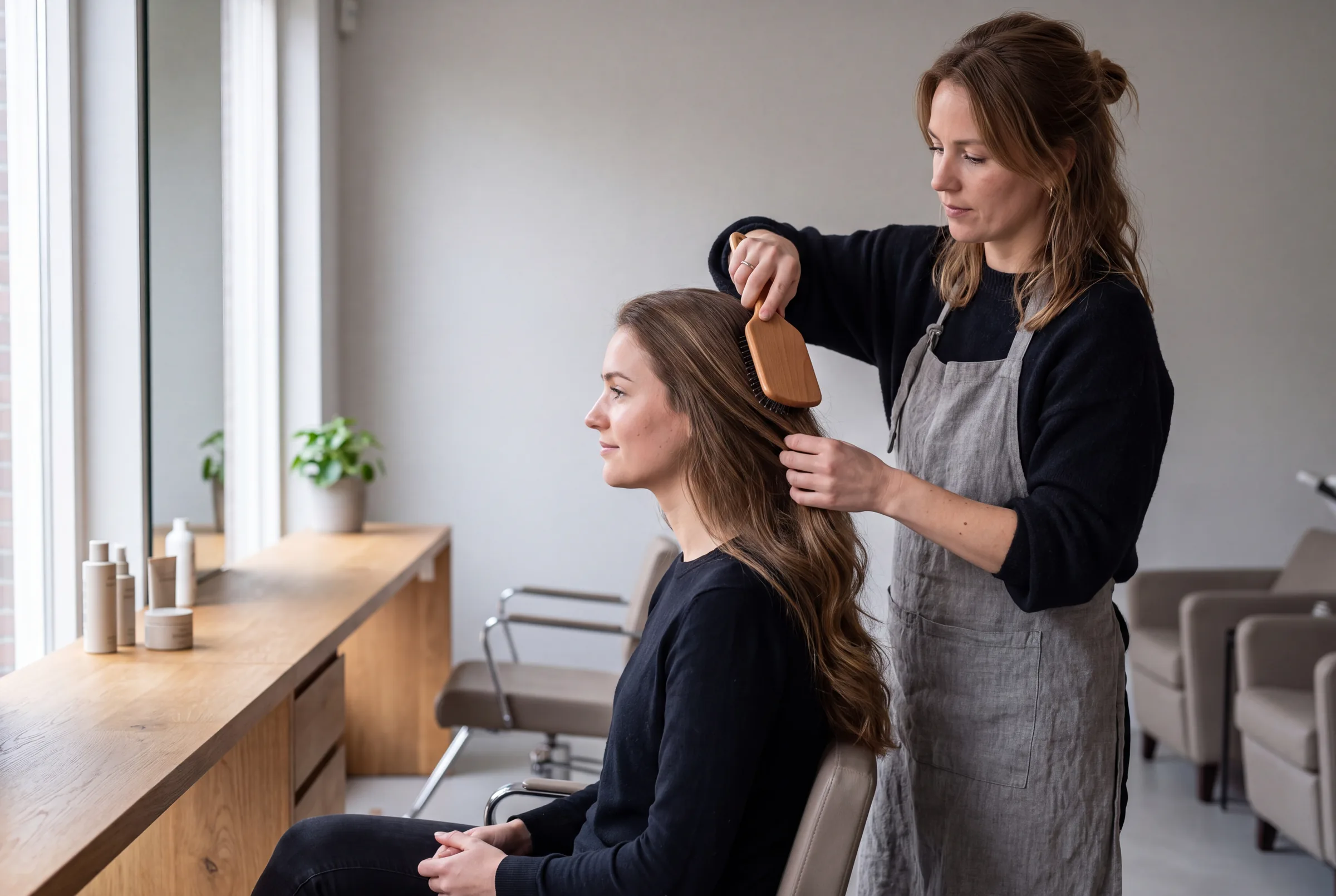 Kapster borstelt het lange haar van een klant in een lichte kapsalon