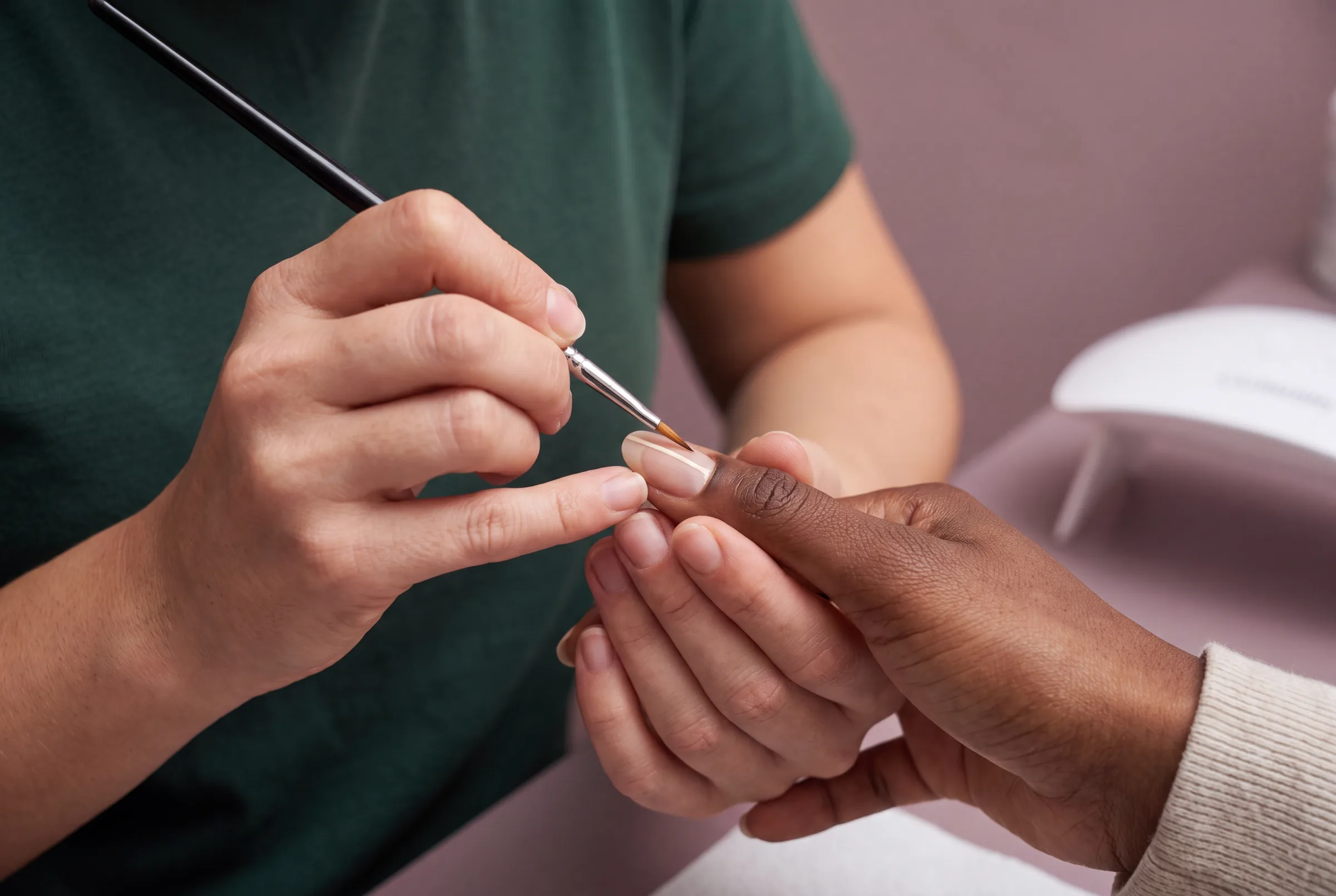 Nagelstylist zet met een fijn penseel een dunne lijn op de nagel van een klant